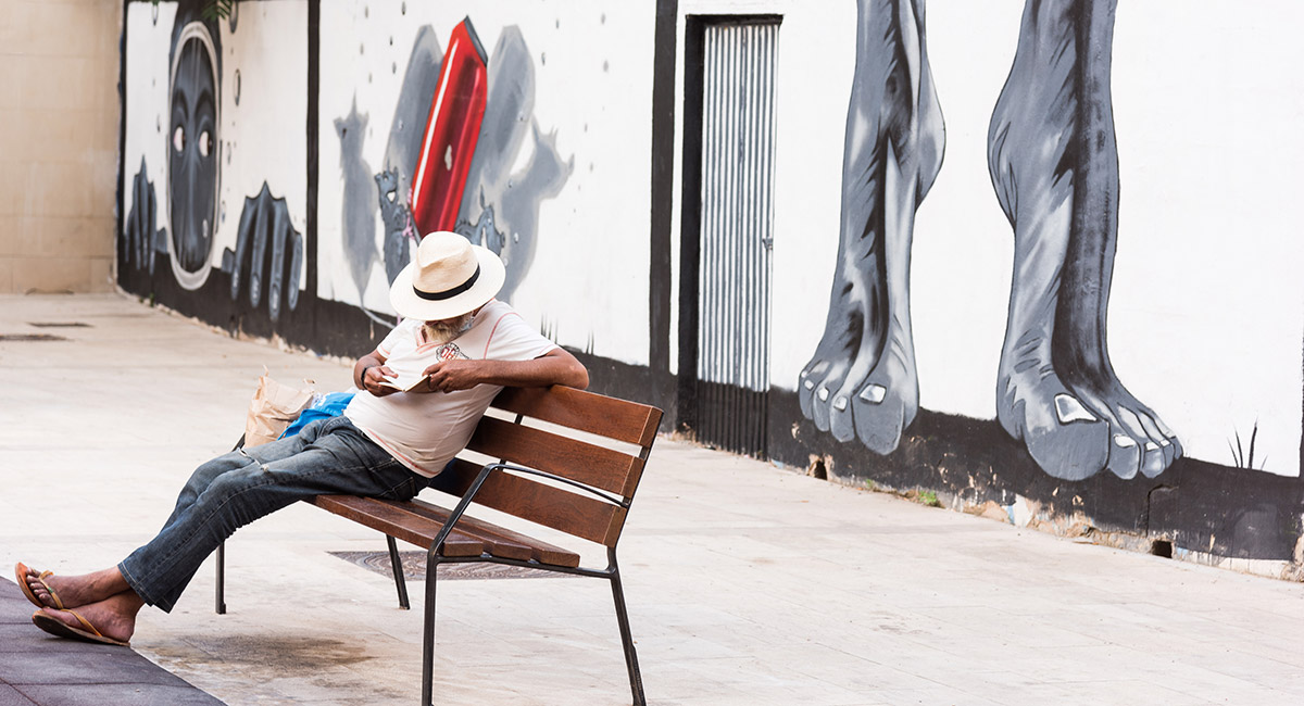 Image of man on bench in Valencia with large feet on mural wall behind him